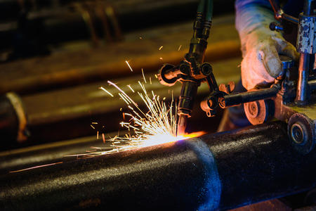 Worker cutting steel pipe with acetylene welding cutting torch and bright sparks in steel...