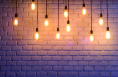 Blurred image of old vintage light bulb glowing on brick wall in cafe. Vintage toneの写真素材