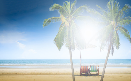 Beach chairs between coconut palm tree on the sand beach with cloudy blue sky backgroundの写真素材
