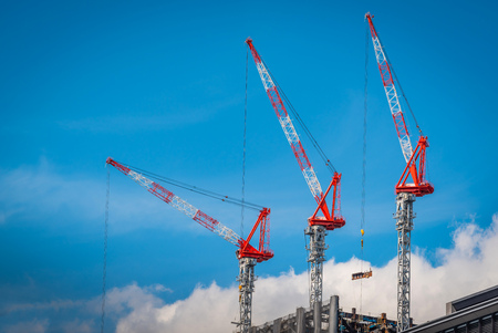 Three construction tower cranes operation at a construction site against blue sky background.の写真素材