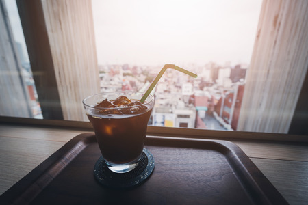 Iced coffee glass cup on wooden table in coffee shop with blurred city background - vintage filterの写真素材