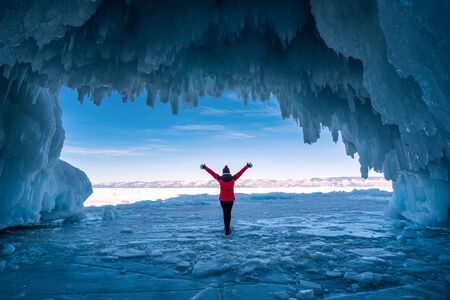 Traveler woman wear red clothes and raising arm standing on frozen water in ice cave at Lake Baikal, Siberia, Russia.の写真素材