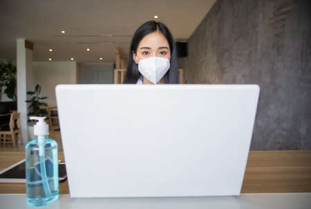Business woman working from home wearing protective mask and using laptop computer. Coronavirus...