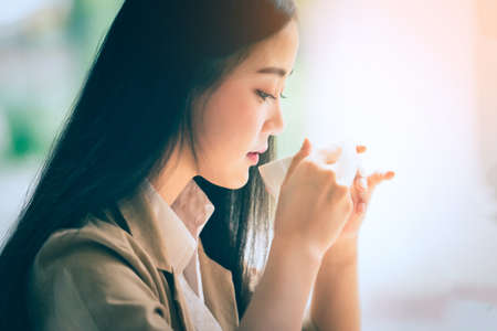 Portrait of Young asian businesswoman sitting indoors in cafe drinking coffee using smart phone. Business success concept.の写真素材