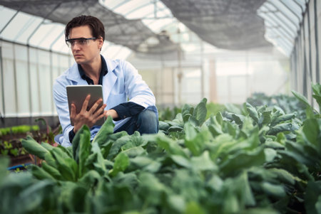 Portrait of handsome agricultural researcher holding tablet while working on research at plantation in industrial greenhouseの写真素材