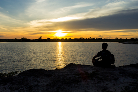 Men sit on the edge of the lake in the evening.の写真素材