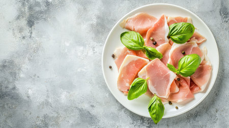 Fresh turkey breast ham slices beautifully arranged on a white ceramic plate with green basil leaves. Top-down view on a gray table with copy space.の素材