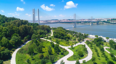 High-altitude drone shot of Vasco da Gama Bridge weaving over the Tagus River, surrounded by lush greenery and urban areasの素材