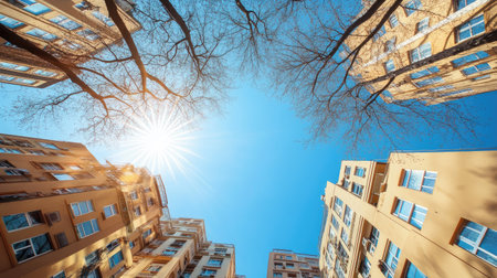 Looking up at a cityscape corner, featuring tall residential buildings and bare winter trees, with the sun shining from the left on a bright blue sky.の素材