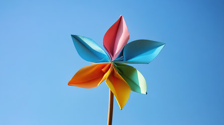 A single multicolored paper windmill on a wooden stick, standing against a clear blue skyの素材