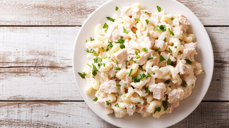 A simple yet elegant white plate of tuna macaroni salad, set on a wooden background with soft natural lighting.の素材