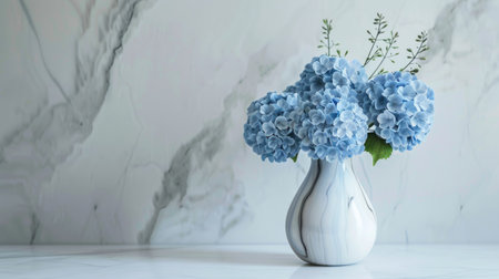 Stylish marble vase with a minimalist shape, holding a refined bouquet of blue hydrangeas and green stemsの素材