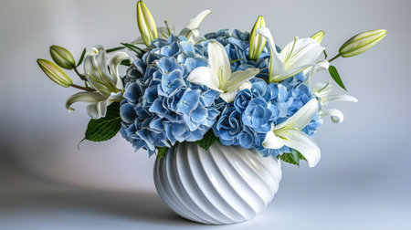 Sleek modern vase with a sculptural design, featuring a fresh mix of blue hydrangeas and white liliesの素材
