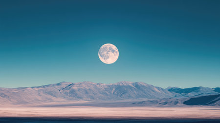 A bright full moon shines brilliantly in the clear blue sky, casting a serene glow over a peaceful landscape with distant mountains.の素材