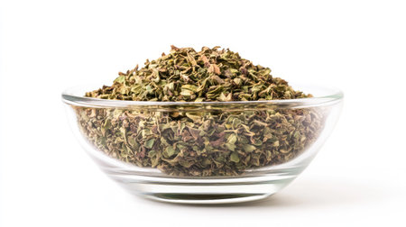 A front view of a glass bowl filled with dried oregano, isolated on a white background, with the vibrant green and brown hues of the herb clearly visible.の素材