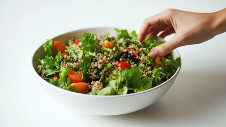 A hand presenting a bowl of quinoa salad with fresh greens, carrots, and tomatoes, with a clean white background emphasizing the vibrant colors of the ingredients.の素材