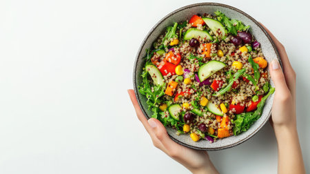 A healthy vegan quinoa salad with organic vegetables, held in a bowl by hand, featuring bright colors and fresh ingredients, shot from the top down on a white background.の素材