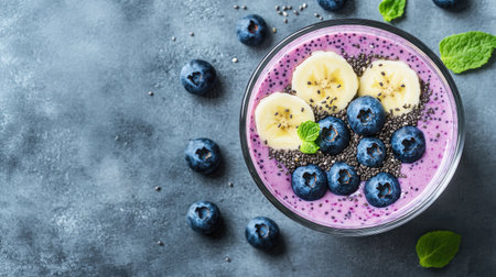 A refreshing smoothie of blueberries, banana, chia seeds, and yogurt in a glass, placed on a sleek gray concrete background.の素材