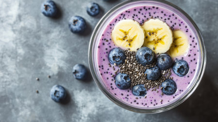 Creamy smoothie with blueberries, banana, chia seeds, and yogurt, served in a glass on a gray concrete background. A nutritious treat.の素材