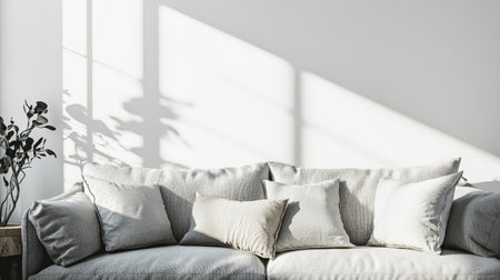 Living room interior with a gray fabric sofa and decorative pillows against a white wall, bright sunlight streaming in, free space on the left for mock-up designの素材