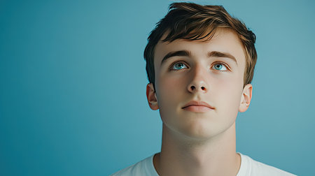 A young man with a thoughtful sideways glance, set against a simple light blue backdrop, capturing the mood of reflection, ideal for lifestyle or motivational themes.の素材