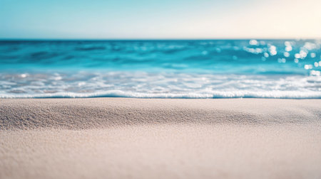 Sunlit beach sand with soft textures in the foreground and a vibrant blue ocean in the background, evoking the perfect summer getaway.の素材