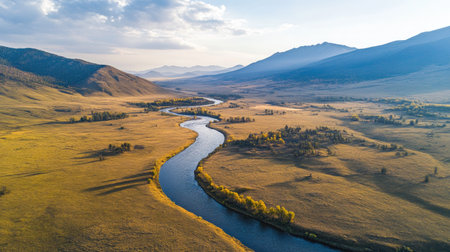 A breathtaking aerial view of a winding river flows through a tranquil mountainous landscape, surrounded by lush greenery and dramatic hills under a clear blue sky.の素材