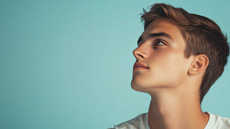 A young man gazes upward with a calm expression against a soft blue background, capturing a moment of thoughtfulness and serenity ideal for lifestyle themes.の素材
