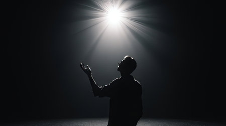 A silhouette of a man reaches toward a bright light in a dark space, symbolizing hope and inspiration. The image conveys emotion, mystery, and ambition.の素材