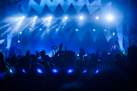 silhouettes of concert crowd in front of bright stage lightsの写真素材