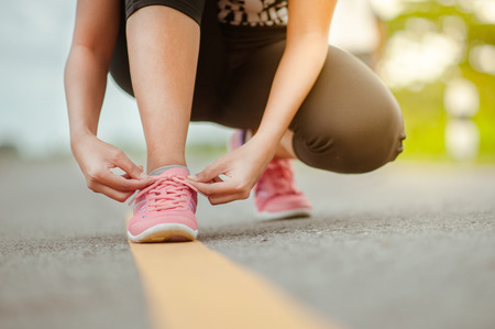 Running shoes - closeup of woman tying shoe laces. Female sport fitness runner getting ready for jogging outdoors on forest path in spring or summer.の写真素材