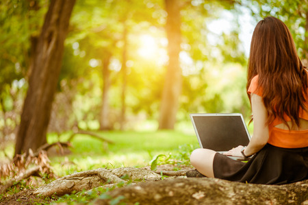woman sitting in park on the green grass with laptop, notebook, hands on keyboard. Computer screen mockup. Student studying outdoors. Copy space for textの写真素材