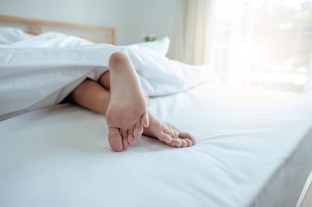 Young female sleeping in bed at home with focus on legs. Feet of woman lying on bed.の写真素材
