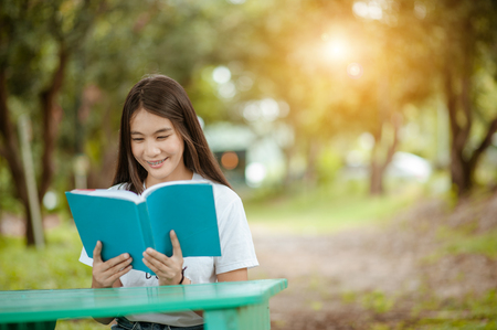 Asian girl reading book at park in summer sunset light. asian woman reading book in Thailand. asian Beautiful woman reading a book at table.の写真素材
