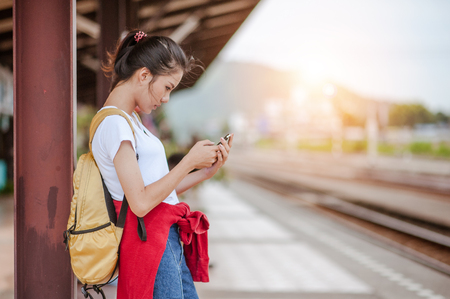 Traveler woman use smartphone and waits train on railway platform.の写真素材