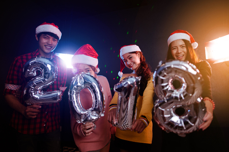 Happy New Year to you! Group of cheerful young people in Santa hats carrying silver colored numbersの写真素材