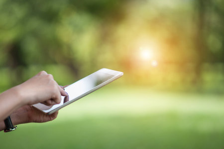 girl using a digital tablet outdoor at the park. Modern technology concept.digitally enhanced. Selective focus on the tablet.の写真素材