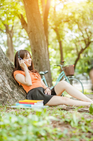 Woman relax and reading a book while listening music with headphone in the nature green park, girl happy.の写真素材