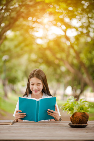 Asian girl reading book at park in summer sunset light. asian woman reading book in Thailand. asian Beautiful woman reading a book at table.の写真素材