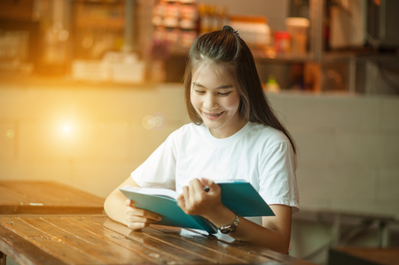 Young woman in a restaurant reading a book.girl sitting by wooden table and reading bookの写真素材