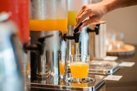 close up hand pulling down the lever of juice dispenser for fresh orange juice.の写真素材