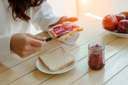 Asian woman slicing jam bread in the morning.feeling happy and fresh.Making breakfast meal in kitchen room.の写真素材