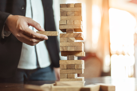 business man hand  pulling out or placing wood block on the tower in modern office. plan and strategy in business. blur for background.の写真素材