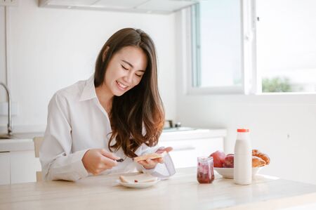 Asian woman slicing jam bread in the morning.feeling happy and fresh.Making breakfast meal in kitchen room.の写真素材