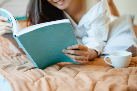 woman reading book and drinking coffee on bed.の写真素材