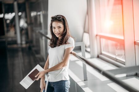 The woman was smiling and holding a travel document and passport in the airport terminal.の写真素材