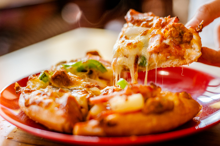 A slice of pizza in hand.Hot pizza slice with melting cheese.の写真素材