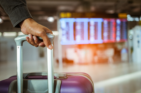 close up man hand touching baggage for check in at flight timetable in international airport.の写真素材
