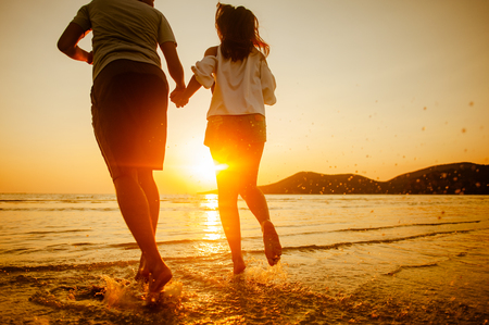 happy couple running to the sea at sunset beach.の写真素材