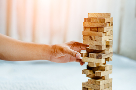 hand  pulling out or placing wood block on the tower in modern office. plan and strategy in business. blur for background.の写真素材